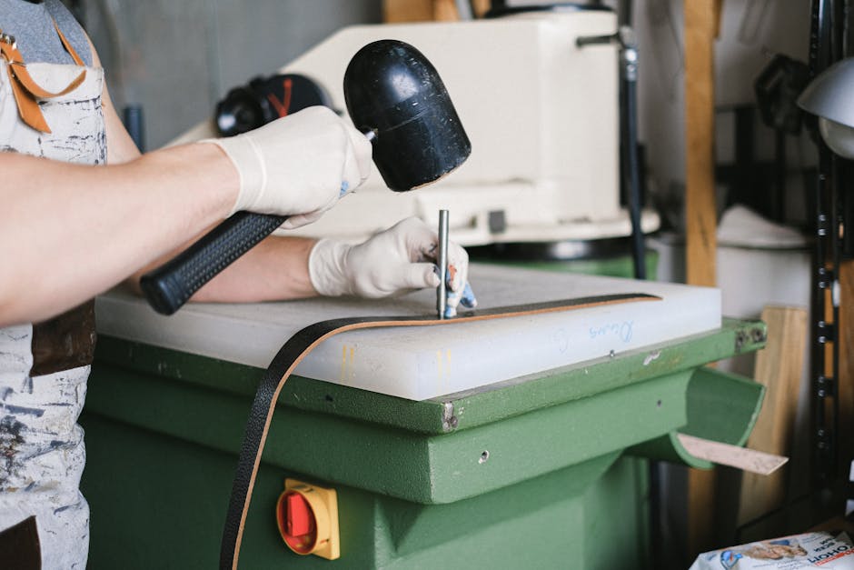 A leather artisan uses a mallet to craft leather goods on a workbench.