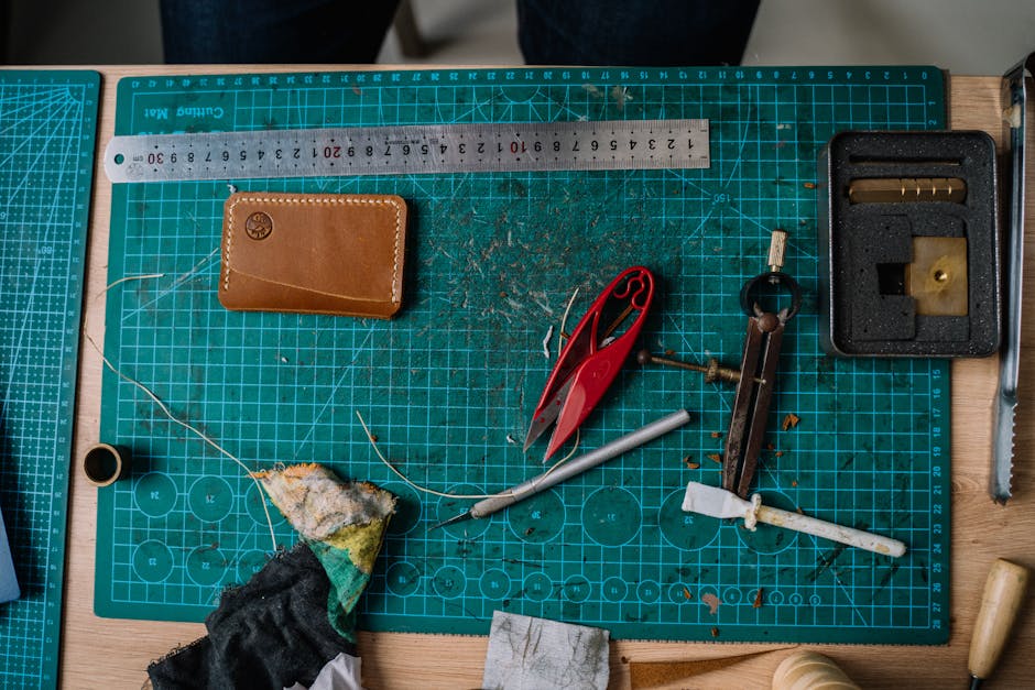 Top view of leather crafting tools including ruler, scissors, and wallet on a work table.
