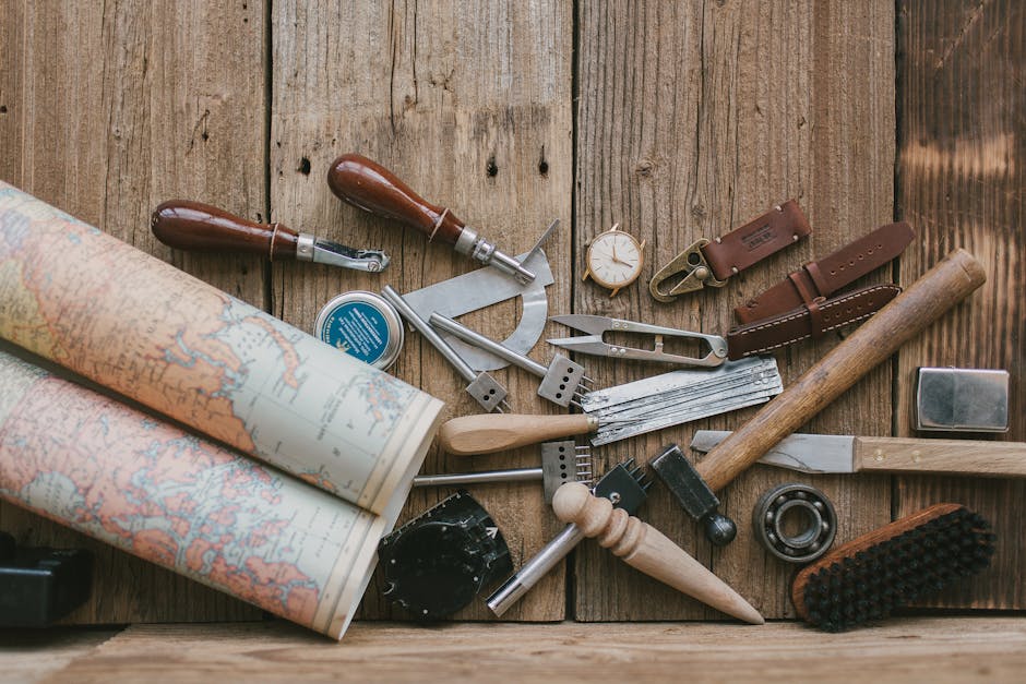 A collection of leather crafting tools on a rustic wooden surface with a world map.