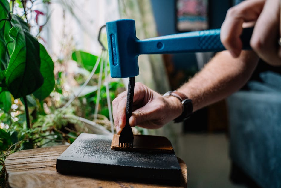 Hands skillfully hammering leather with tools in a studio setting surrounded by greenery.